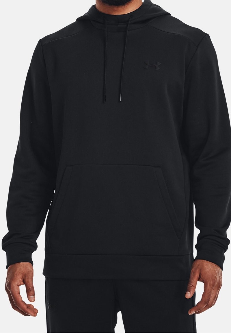 Homme portant un sweat à capuche noir Under Armour avec cordons et une poche kangourou à l'avant, debout devant un fond uni.