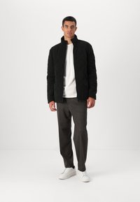 Μαύρο επενδυμένο μπουφάν με ψηλό γιακά, μπροστινό φερμουάρ και πλαϊνές τσέπες. Φορεμένο πάνω από λευκό t-shirt και συνδυασμένο με γκρι παντελόνι και λευκά αθλητικά παπούτσια.