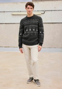 Dark gray knitted sweater with a geometric white pattern, paired with light beige pants and gray sneakers, showcasing a casual outfit.