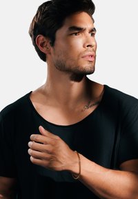 Gold chain bracelet worn on the wrist of a person with a short-sleeved black shirt. The background is plain, enhancing the focus on the accessory.