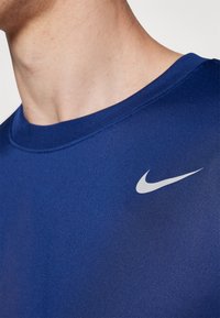 T-shirt de sport Nike bleu avec un col rond, texture lisse et logo blanc sur la poitrine. Le tissu semble léger et respirant.