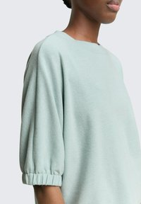 Hellgrüner, strukturierten Pullover mit einem Bootsausschnitt, puffäermigen Kurzärmeln und gerafften Manschetten. Der Stoff wirkt weich und lässig im Stil.