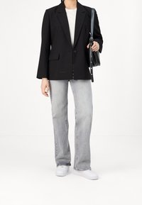 Svart blazer med en enda knapp, notch slag och två framfickor, kombinerad med ljusgrå utsvängda jeans och vita sneakers.