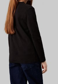 Černý dlouhý rukáv tričko z bavlny, s kulatým výstřihem a přiléhavým střihem. V kombinaci s tmavě modrými džíny.