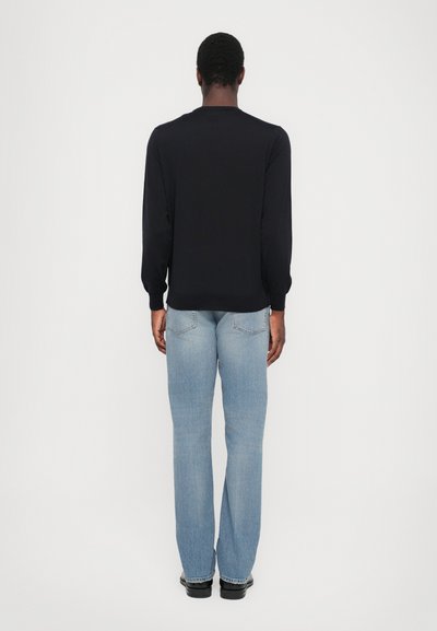 Black long-sleeve shirt paired with light blue straight-leg jeans. The outfit features a relaxed fit and minimalistic design, without embellishments.