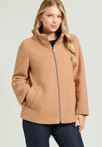 Giacca in pile marrone con colletto alto, zip frontale e tasche laterali. Materiale morbido e dalla texture con vestibilità ampia e taglio dritto.