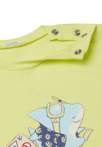 T-shirt in cotone giallo fluo con grafica di uno squalo, scollatura rotonda e dettagli con bottoni a pressione sulla spalla per un facile indossare.