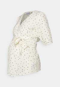 Top avvolgente bianco con pois neri, maniche corte a sbuffo e vita legata. Realizzato in tessuto leggero, adatto per l'abbigliamento premaman.