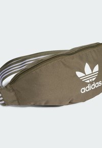 Riñonera de tela verde oliva con cierre de cremallera, logo de Adidas en blanco y correa ajustable a rayas para un ajuste seguro.