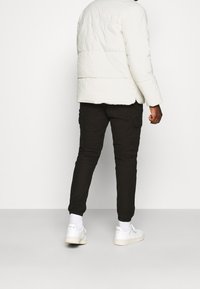 Chaqueta de plumas blanca con textura acolchada, combinada con pantalones cargo negros y zapatillas blancas. El conjunto presenta un ajuste casual y relajado.