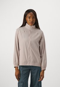 Veste zippée rose clair avec un col haut, une taille élastique et des poches latérales ; fabriquée en tissu lisse et léger avec une coupe décontractée.
