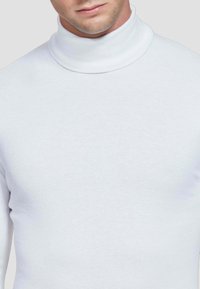 Maglione bianco a collo alto in un tessuto morbido con una vestibilità aderente, caratterizzato da un colletto alto e una superficie liscia, con dettagli delle cuciture visibili.
