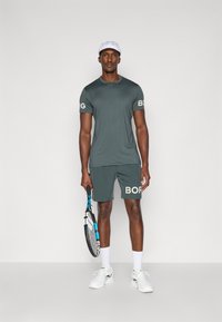 Sportowy strój w ciemnoszarym kolorze, składający się z koszulki z krótkim rękawem i szortów, z akcentami logo "BORG". Wyposażony w rakietę tenisową.