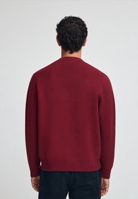 Roter Pullover mit strukturiertem Strickmuster, Rundhalsausschnitt und gerippten Bündchen und Saum. Das Design zeichnet sich durch eine lässige Passform aus und wird von hinten gezeigt.