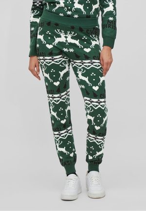 Gambe con pantaloni verdi a tema natalizio ricamati con renne bianche, cuori, alberi e la scritta "Buon Natale", abbinati a scarpe da ginnastica bianche.