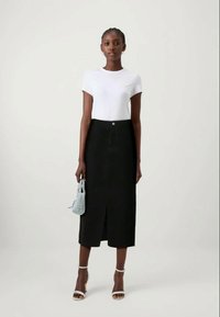 T-shirt blanc à manches courtes associé à une jupe midi noire avec une fente frontale, complété par un sac à main bleu clair et des talons blancs à lanières.