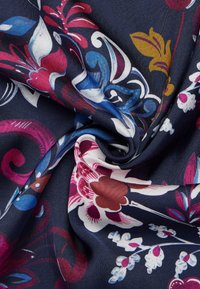 Tessuto blu navy con motivi floreali in rosso, rosa, blu e giallo, caratterizzato da disegni ondulati e una texture liscia e lucida.