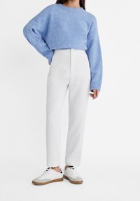 Maglione lavorato a maglia azzurro chiaro, pantaloni bianchi a vita alta e sneakers bianche con dettagli grigi. L'outfit presenta una vestibilità comoda e un tessuto testurizzato.