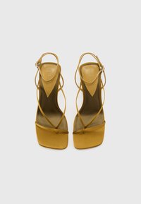 Sandales à talons jaunes à brides, avec un bout carré, fabriquées en matière lisse, équipées de brides croisées et d'une boucle fine au niveau de la cheville.