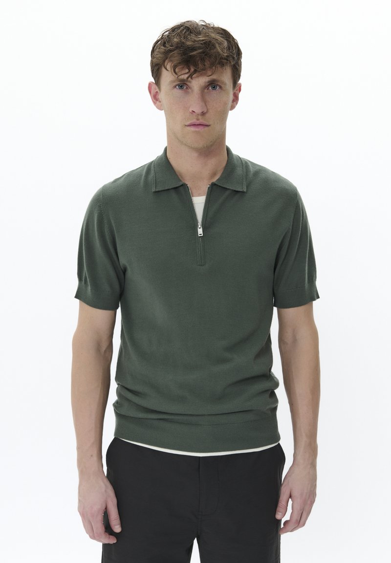 Polo de manga corta de color verde oscuro con cuello con cremallera, hecho de una tela de punto suave. Presenta mangas ajustadas y un corte relajado.