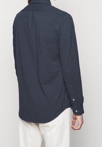 Marinblå skjorta med vita prickar, långa ärmar, knäppning vid ärmsluten och en lätt svängd nederkant. Tillverkad av ett mjukt, lätt tyg.