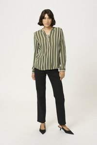 Long-sleeve olive green shirt with vertical white stripes, collarless neckline, and black fitted pants. Black pointed-toe heels.