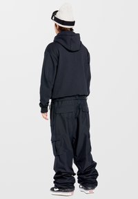 Sort hættetrøje med en afslappet pasform, parret med løse sorte cargo-bukser med flere lommer. Grå hue og sneakers.