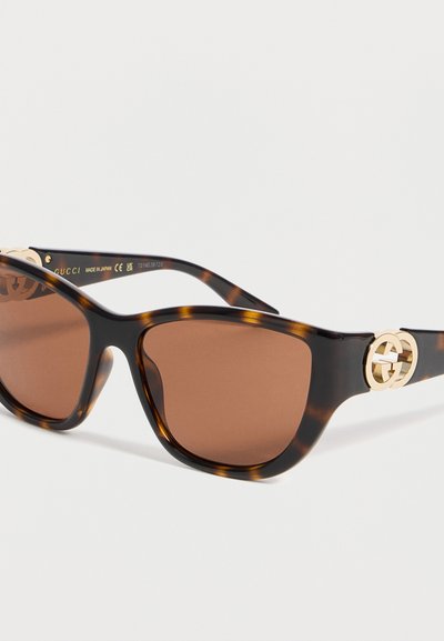 Γυαλιά ηλίου με σχήμα ματιού γάτας και σχέδιο χελώνας, καφέ φακούς και χρυσό λογότυπο Gucci στον βραχίονα, κατασκευασμένα στην Ιαπωνία.