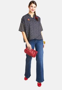 Dunkelblaue Bluse mit gemusterten Ärmeln, kombiniert mit hellblauen Schlagjeans. Accessoires mit einer roten Clutch und roten Schuhen.