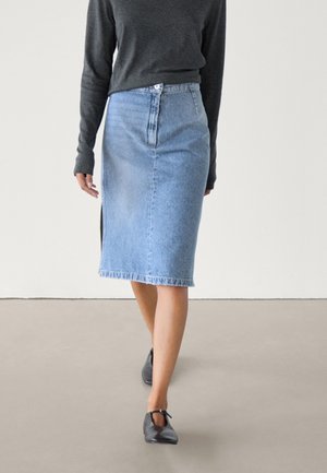 Woman walking wearing a light blue denim knee-length skirt, dark gray long-sleeve top, and black flat shoes with ankle straps.
