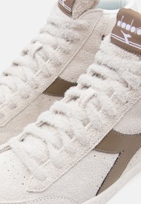 White suede high-top sneakers with fuzzy texture, brown leather accents, stitched detailing, and flat shoelaces. Classic design elements featured.
