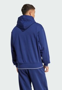 Mörkblå hoodie med en stor huva, med ribbade mudd och nederkant, tillverkad av ett mjukt tyg med subtil struktur och kontrasterande vita detaljer.
