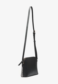 Svart läder crossbody-väska med dragkedjestängning, justerbar rem och strukturerad svart och vit mönstrad sidoprydnad.