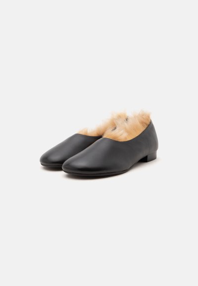 Chaussures en cuir noir à enfiler avec talons bas et doublure en fourrure beige à l'intérieur, présentées sur un fond uni gris clair.