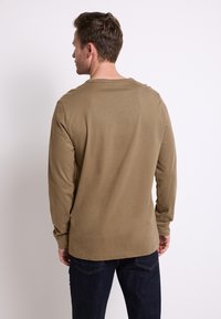 Dlouhý rukáv košile v jemné béžové bavlně, s kulatým výstřihem a rovním lemem, spárovaná s tmavě modrými džíny s klasickým pětipocketovým designem.