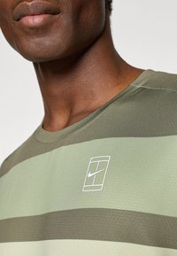 Tricou Nike cu maneci scurte, având dungi orizontale de culoare măslinie și verde, decolteu rotund și un logo alb Nike pe piept.