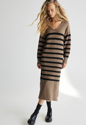 Robe tricotée avec un décolleté en V, des manches longues, un corps beige avec de larges rayures noires, une texture côtelée et des fentes sur les côtés au niveau de l'ourlet.
