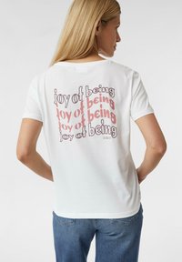 Weißes Baumwoll-T-Shirt mit einem mehrfarbigen "Freude am Sein"-Grafik auf der Rückseite, in verschiedenen Schriftgewichten und -stilen. Klassischer Rundhalsausschnitt.