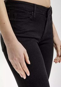 Czarne dżinsy o dopasowanej sylwetce, z zamkiem błyskawicznym, szlufkami na pasek i kieszeniami z przodu, prezentowane na poziomie talii i ud.