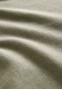 Close-up af beige stof med synlig fin strikstruktur og bløde folder, der skaber blide skygger.