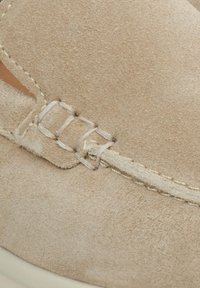 Beige Wildlederschuh mit einer gestickten Design und einem dekorativen Riemen mit doppelten Schnallen. Die Sohle ist hell gefärbt und leicht erhöht.