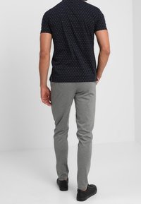 Marinblå kortärmad polo med vita prickar, grå slim-fit sweatpants och svarta sneakers. Slät textur och avslappnad design.