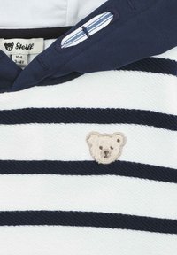 Felpa a strisce bianche e blu navy con cappuccio, che presenta un piccolo emblema di un orso ricamato. I materiali sembrano morbidi con un tessuto testurizzato.