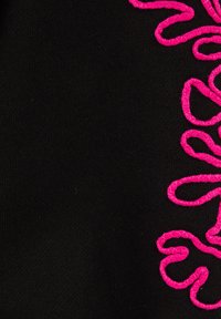 Melns audums ar teksturētu virsmu, kurā redzams spilgti rozā izšuvums, kas veido plūstošu rakstu labajā pusē.