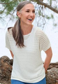 Lichtgewicht, crèmekleurig gebreid topje met korte mouwen en horizontale strepen, gedragen over een witte tanktop, gecombineerd met blauwe jeans.