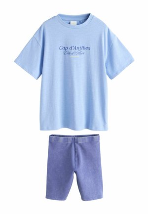 Jasnoniebieska koszulka z krótkim rękawem z napisem „Cap d’Antibes Côte d’Azur” w zestawie z jednolitymi fioletowymi szortami do kolan.