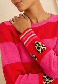 Pulover tricotat cu dungi în roșu, roz și fucsia; are accente cu imprimeu de leopard pe mâneci și un finisaj texturat.