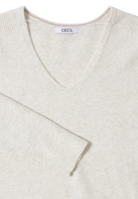 Witte V-hals trui van zachte gebreide stof. Voorzien van geribbelde mouwen en een label met de tekst "CECIL" bij de halslijn. Naadloos ontwerp.
