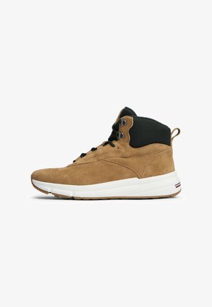 Bruine suède hoge sneaker met zwarte gewatteerde kraag, zwarte veters, witte zool en een trekhaak bij de hiel, zijaanzicht.