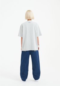 Light grey cotton t-shirt with short sleeves and relaxed fit, paired with loose-fitting, dark blue denim pants. Minimalistic design.